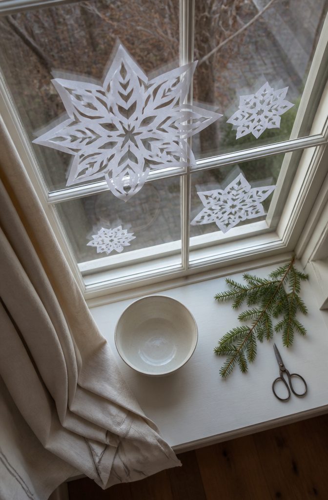 White paper snowflakes cut into symmetrical patterns and taped to a window